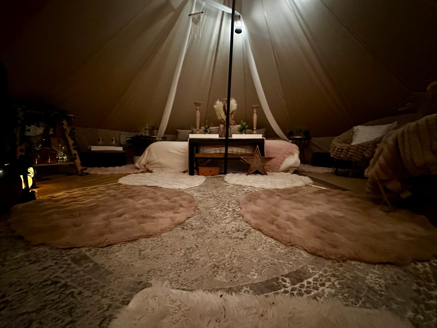 Wide bell tent interior with layered rugs, a wooden star marquee, pampas and soft neutral styling.