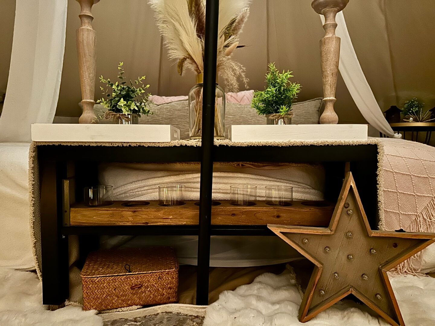 Under-bed styling detail with marquee wood star, woven basket, candles and pampas grass.
