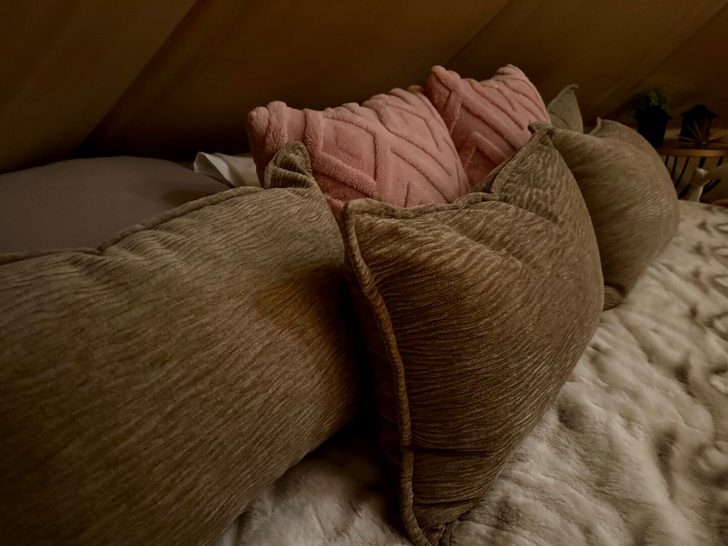 Close detail of pink and sage pillows layered on a bell tent bed.
