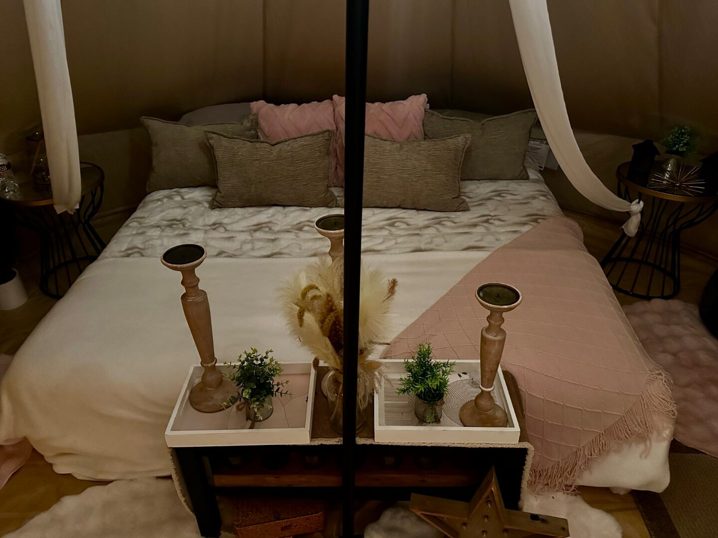 Close detail of bell tent bedding with pink and sage pillows and wooden candlesticks.