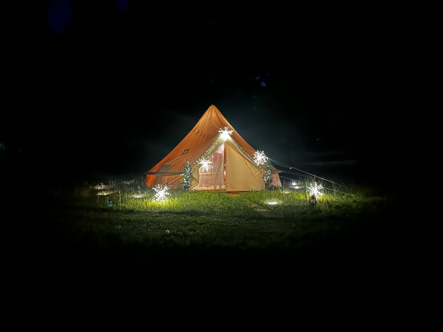 Bell tent exterior at night with ground-level sparkler lights around the entrance.